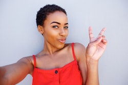 Portrait of young woman taking selfie with peace hand sign