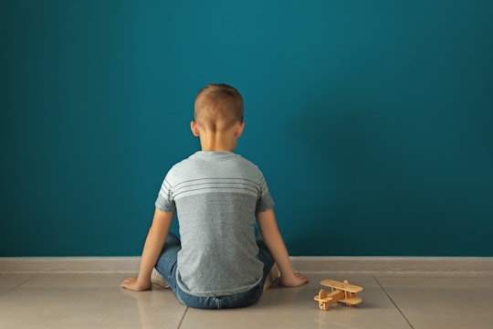 Little boy sitting near dark wall in empty room. Autism concept