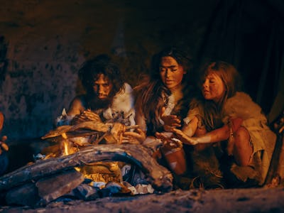 Neanderthal or Homo Sapiens Family Cooking Animal Meat over Bonfire and then Eating it. Tribe of Pre...