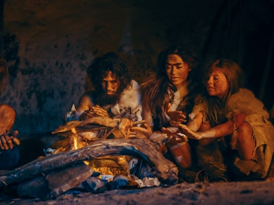 Neanderthal or Homo Sapiens Family Cooking Animal Meat over Bonfire and then Eating it. Tribe of Pre...
