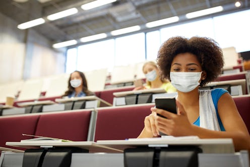 education, healthcare and pandemic concept - african student girl wearing face protective medical ma...