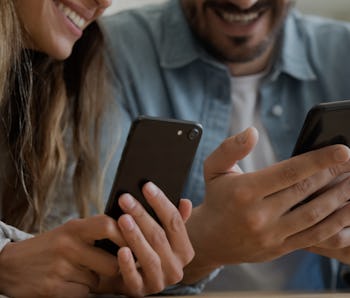 Close up happy family couple using smartphones, sharing contacts or funny content, watching photos o...