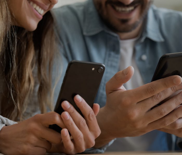 Close up happy family couple using smartphones, sharing contacts or funny content, watching photos o...