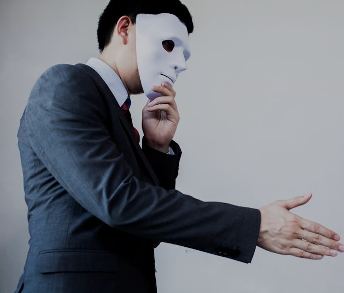 Business man giving dishonest handshake hiding in the mask.