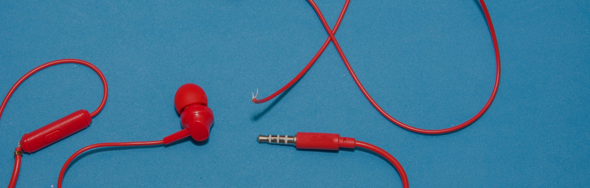 Red broken torn headphones on classic blue background. 