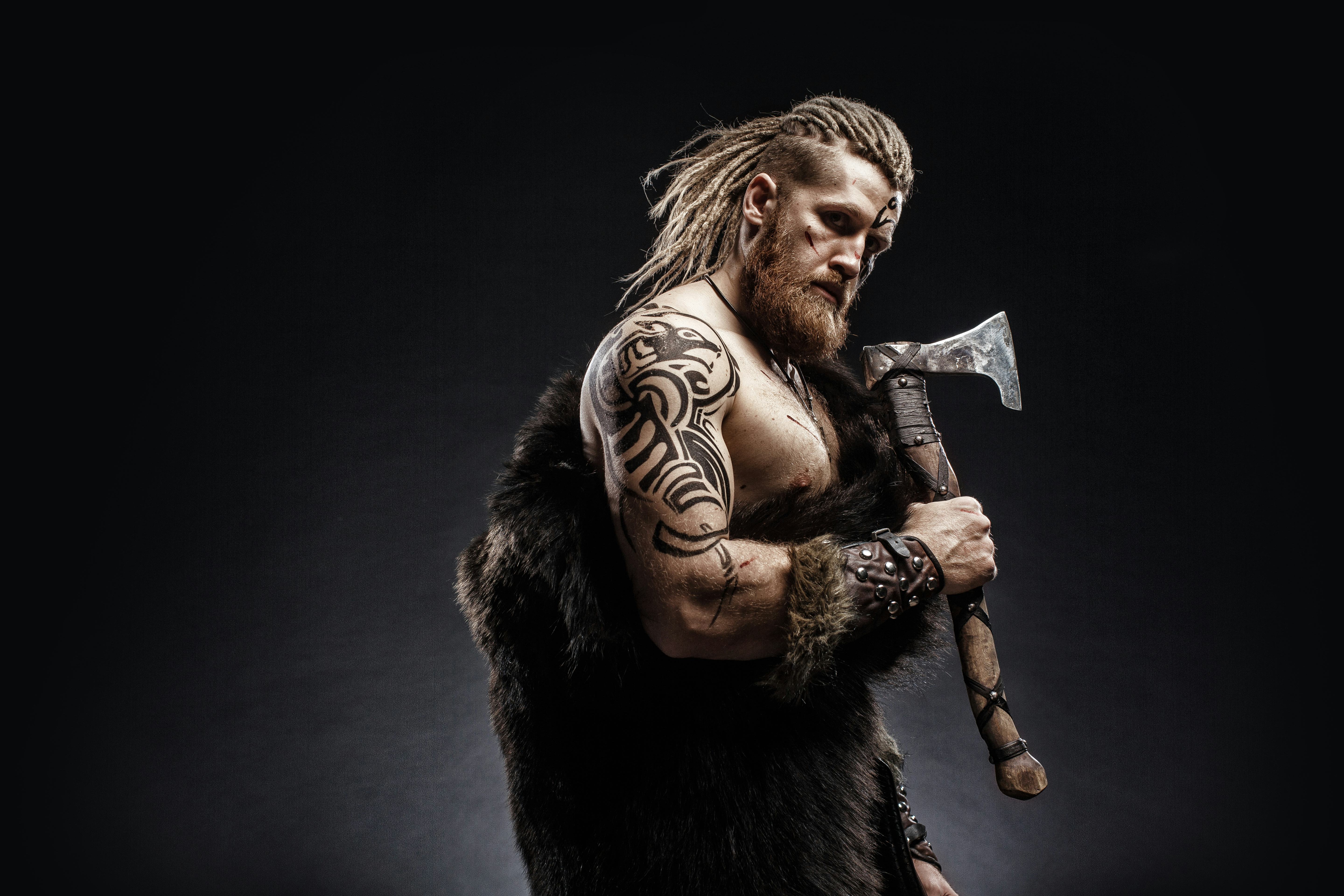 Medieval warrior berserk Viking with tattoo with axes attacks enemy. Concept historical photo
