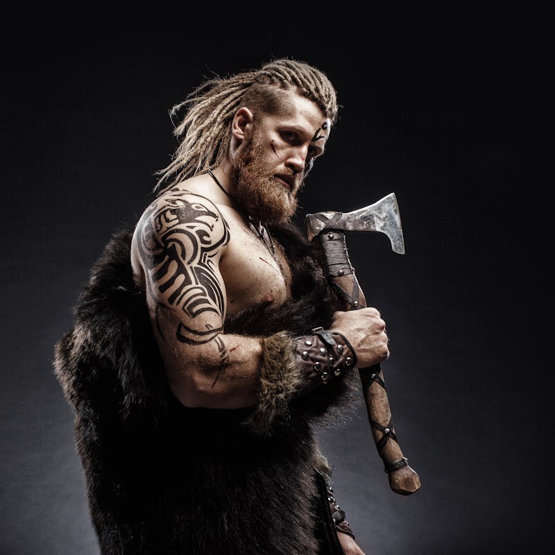 Medieval warrior berserk Viking with tattoo with axes attacks enemy. Concept historical photo