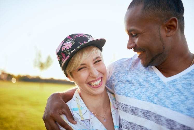 Mixed race couple of millennials in a grass field cuddling and showing affection together