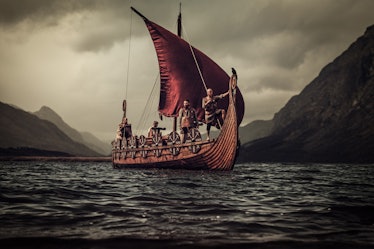 Group of vikings are floating on the sea on Drakkar with mountains on the background.