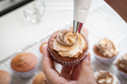 female hands holding piping bag filled with cream cheese and coffee frosting decorating cupcakes