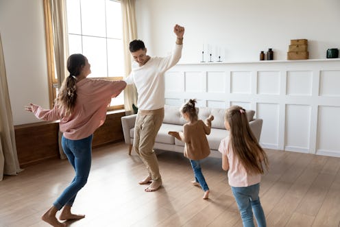 Funny active family of four young adult parents and cute small children daughters dancing together i...