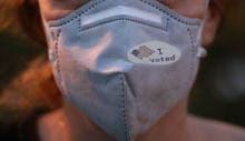 Selective focis on I Voted sticker with USA flag on face mask on caucasian female after voting for p...