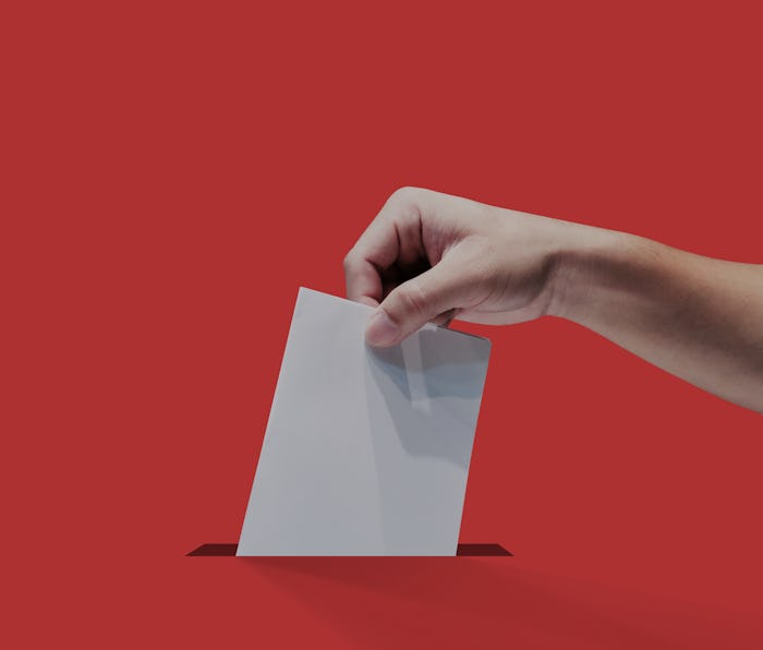 A hand can be seen holding ballot paper for election vote. The paper is white, the background is red...