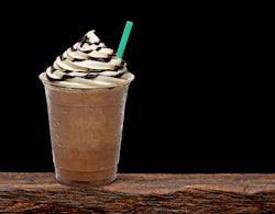 Iced coffee or frappuccino with cream in takeaway disposable cup on wooden table with black backgrou...