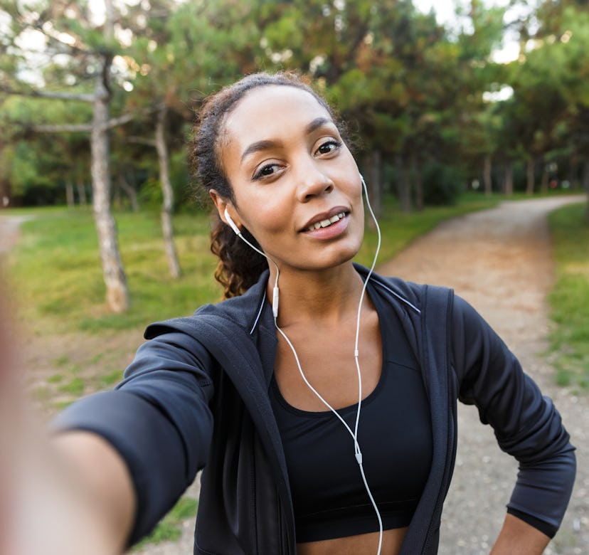 Portrait of pretty woman 20s wearing black tracksuit and earphones taking selfie photo on cell phone...