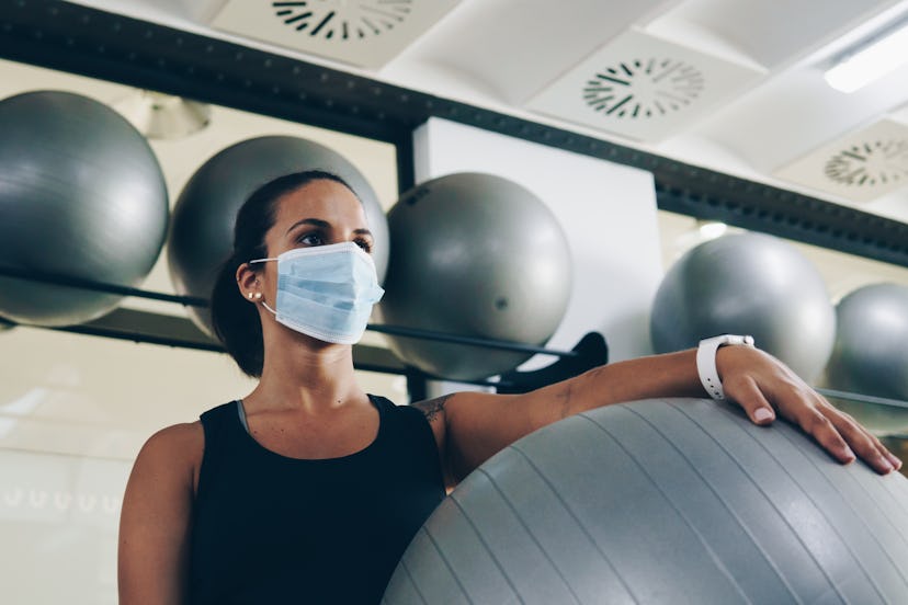 A person wearing a mask carries a yoga stability ball with one arm in the gym. It might be tough, bu...