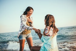 Woman proposing to her happy girlfriend on the beach