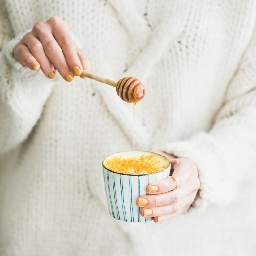 Healthy vegan turmeric latte or golden milk with honey in female hands, square crop