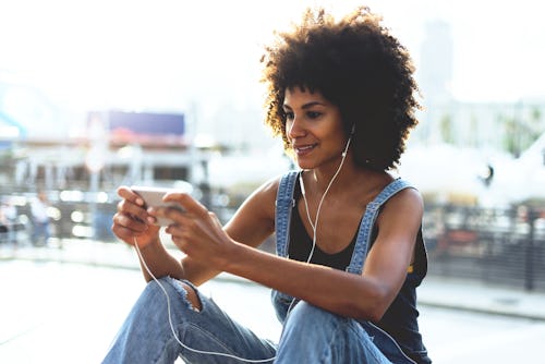 An attractive young dark-skinned girl looking at video on mobile phone while relaxing outside in sum...