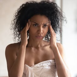 Thoughtful african American woman look in mirror in bathroom worry about facial wrinkles think of an...