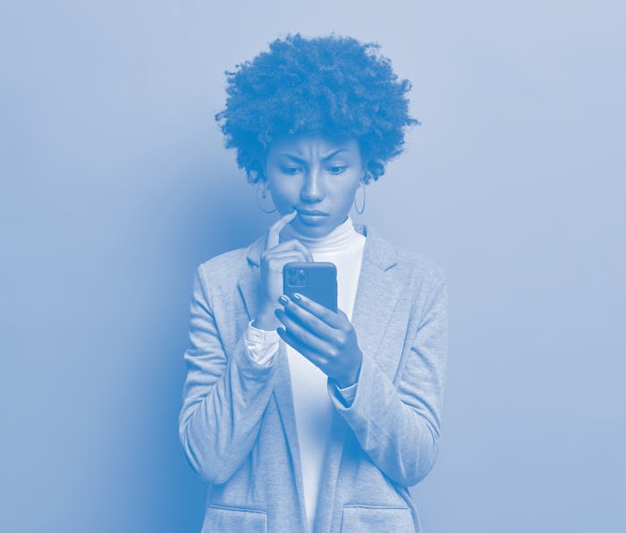 Puzzled confused dark skinned woman in formal wear looks indignant at smartphone, gazes at display, ...