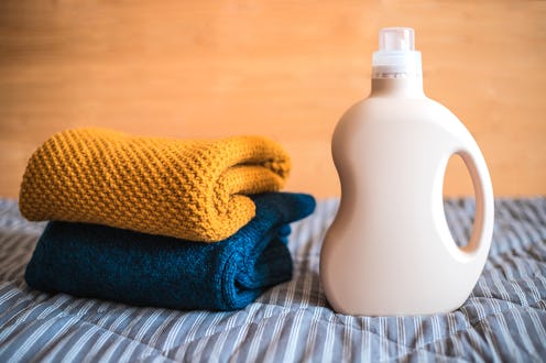 Bottle of detergent and a pile of clean colored sweaters on the bed at home.