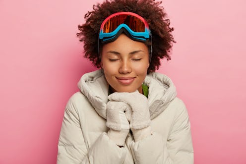 Feeling reaxed and happy. Healthy adorable woman with curly hair, wears white down padded coat and m...