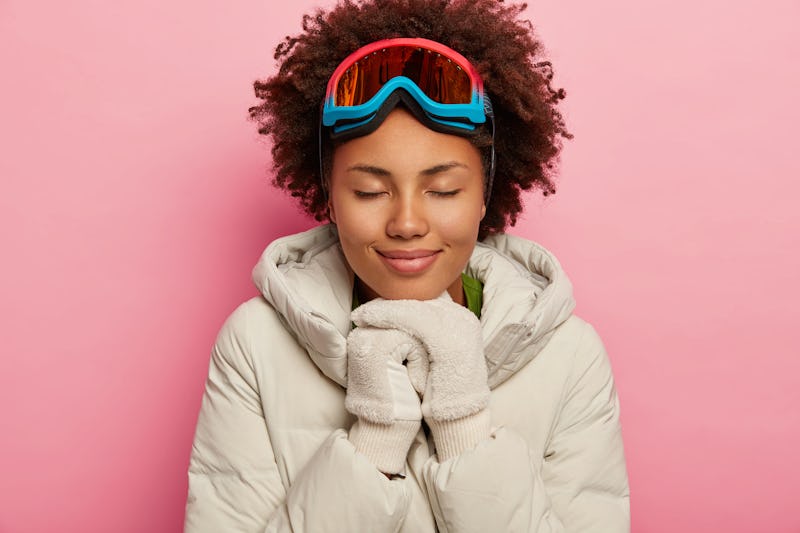Feeling reaxed and happy. Healthy adorable woman with curly hair, wears white down padded coat and m...