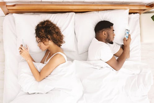 Millennial couple in quarrel, lying on bed back to back, using smartphones. Indifferent and do not p...