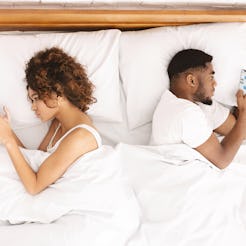 Millennial couple in quarrel, lying on bed back to back, using smartphones. Indifferent and do not p...