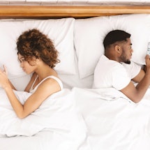 Millennial couple in quarrel, lying on bed back to back, using smartphones. Indifferent and do not p...