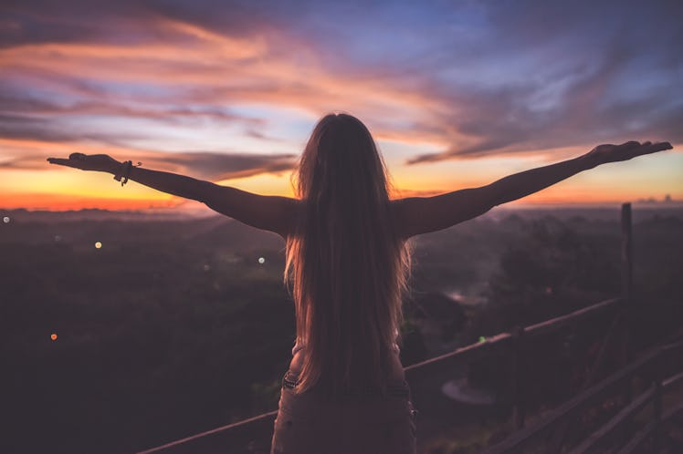 Silhouette of the woman spreading arms and standing high on the viewpoint with breathtaking view ove...