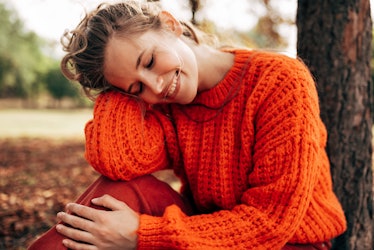 Outdoor image of a attractive young woman smiling, wearing orange knitted sweater posing on fall nat...