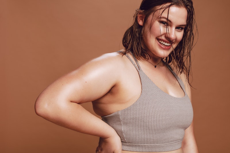 Plus size female model in sports bra looking at camera and smiling. Positive oversized young caucasi...