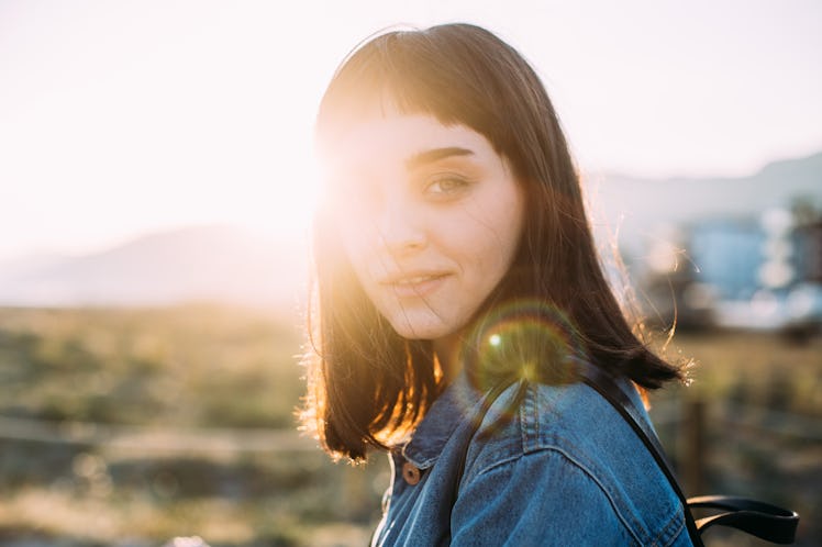 Portrait of a small hipster girl with dark hair and bangs wearing denim jacket and backpack, student...