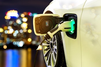 EV Car or Electric car at charging station with the power cable supply plugged in on blurred Night c...