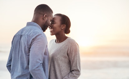 Smiling young African couple talking and laughing together while standing face to face on a beach at...