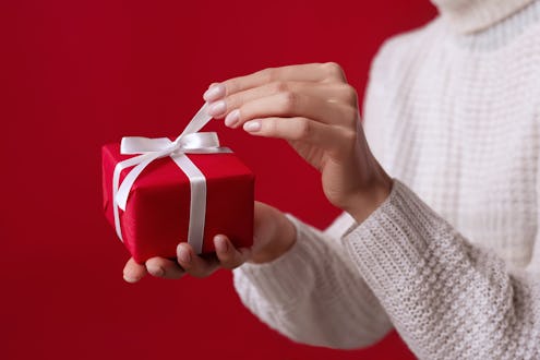 Female hands open Christmas red gift box with white bow on the red background. White sweater. New Ye...