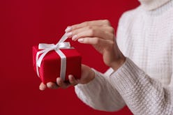 Female hands open Christmas red gift box with white bow on the red background. White sweater. New Ye...