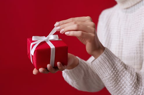 Female hands open Christmas red gift box with white bow on the red background. White sweater. New Ye...