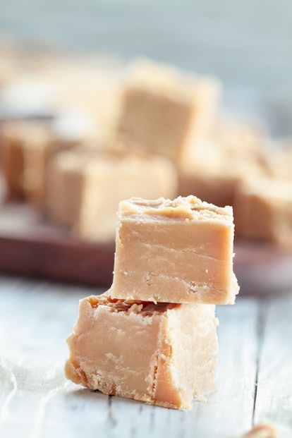 Squares of delicious, homemade peanut butter fudge over a rustic wood table background. Selective focus on stacked candy with blurred background. 