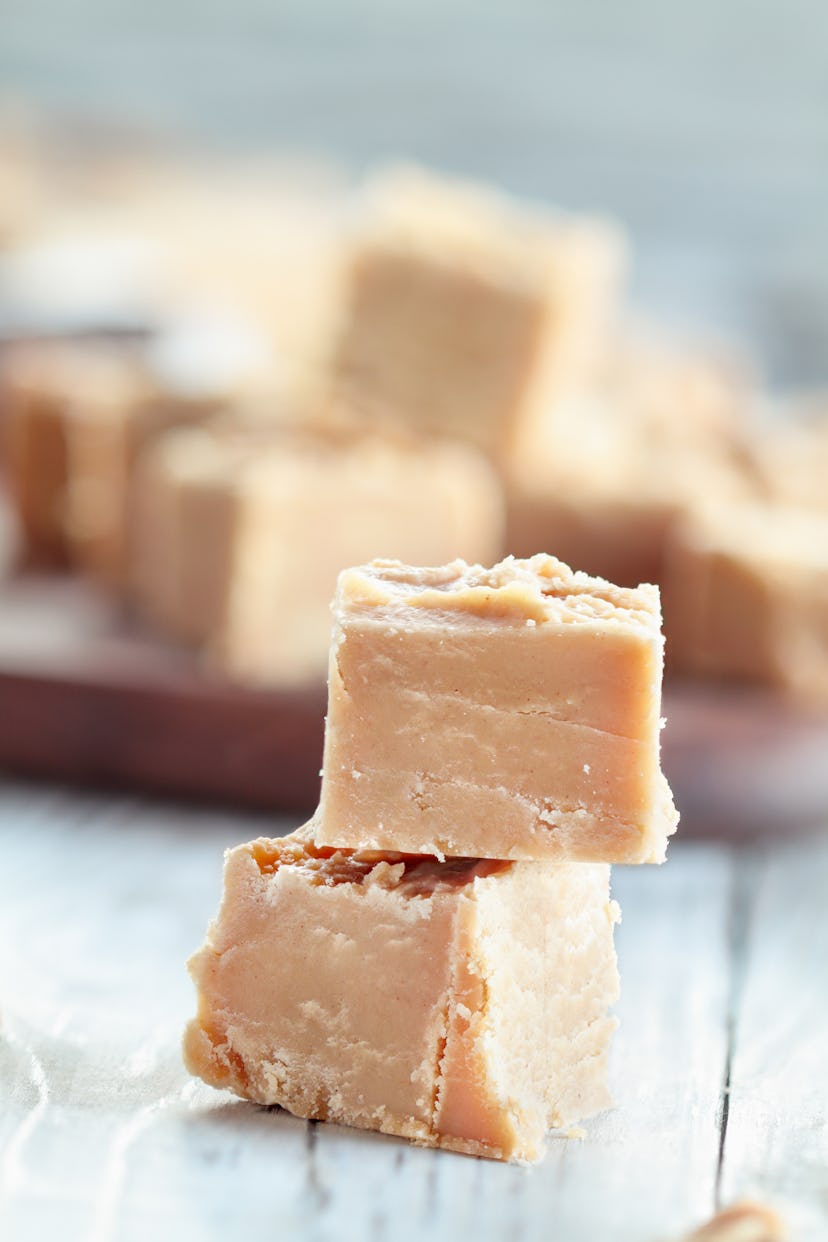 Squares of delicious, homemade peanut butter fudge over a rustic wood table background. Selective fo...