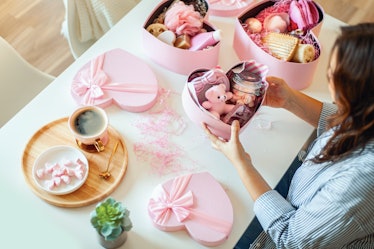 A woman prepares a pink heart-shaped gift basket with a teddy bear and products for her friend on Va...