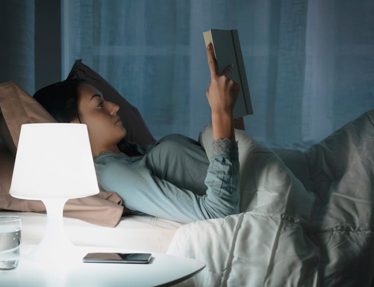 Young beautiful woman lying in bed and reading a book late at night