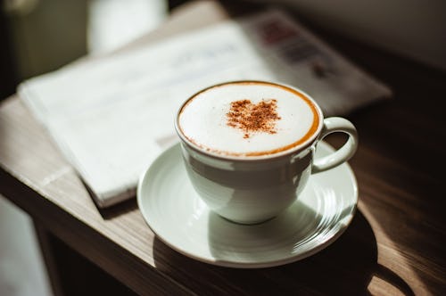 Two cups of cappuccino with latte art on wooden background and newspaper. Cup of cappuccino with new...