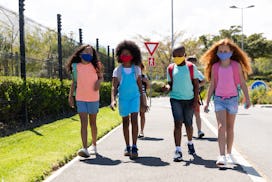 Multi ethnic group of school children wearing face masks, walking on the street. Education back to s...