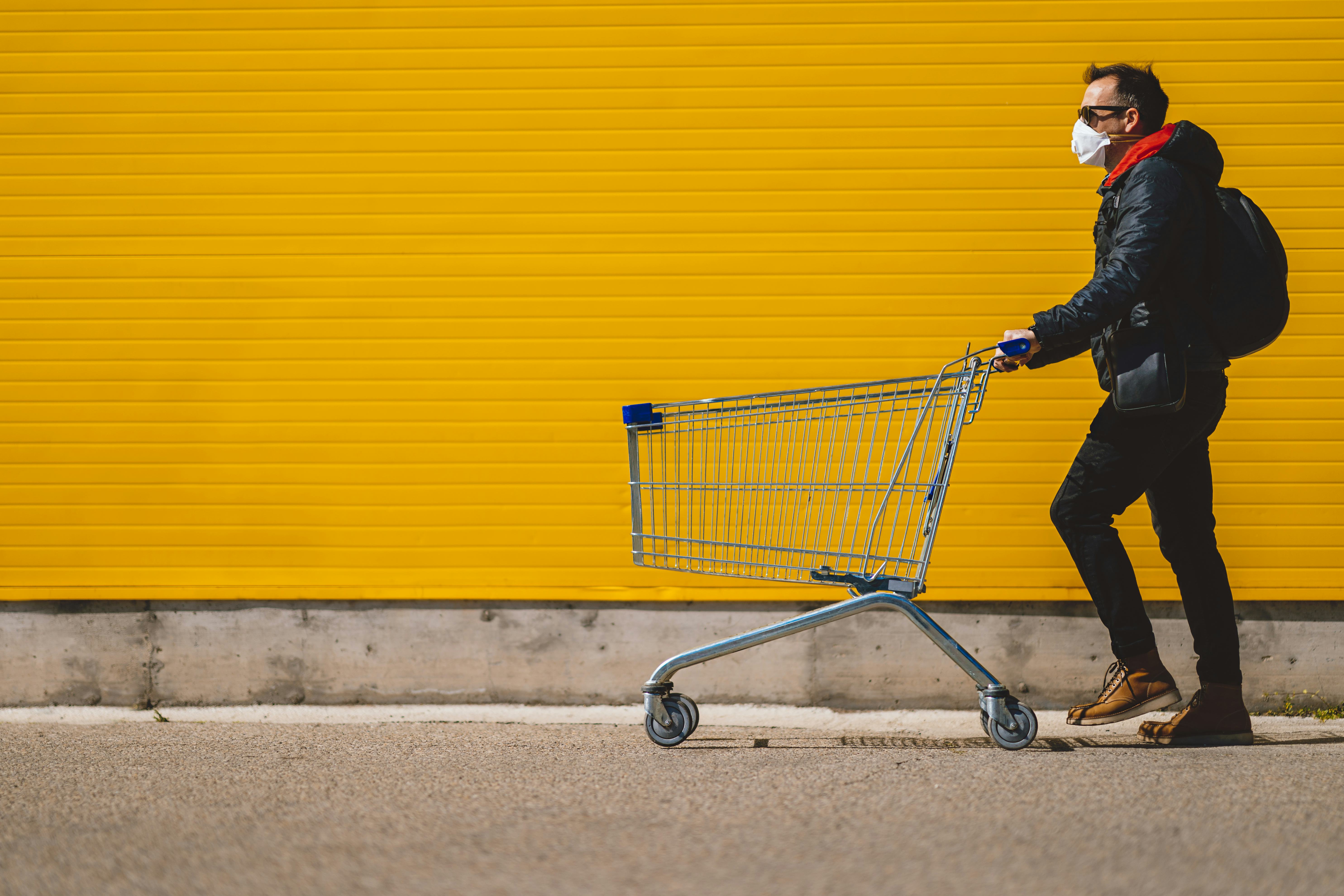 Man with with a shopping cart in front of a store, wearing a mask during a coronavirus pandemic / Co...