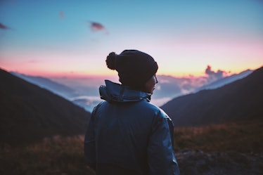 A young woman hiker in a blue jacket standing on peak in the mountains enjoying sunset, amazing view...