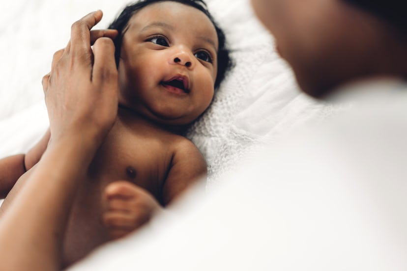 Image of a young newborn baby lying down, looking up at an adult.