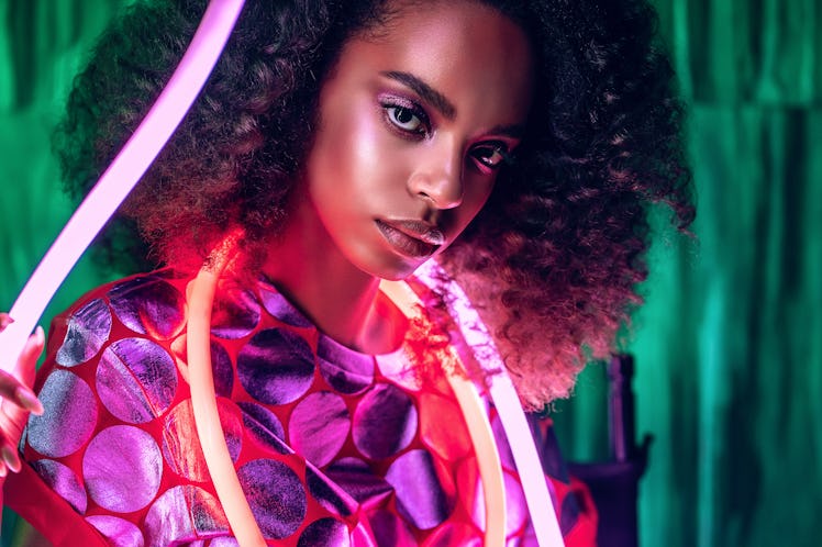 Portrait of african girl in pink top with pink neon light. Woman with afro hairstyle. Pink and red f...